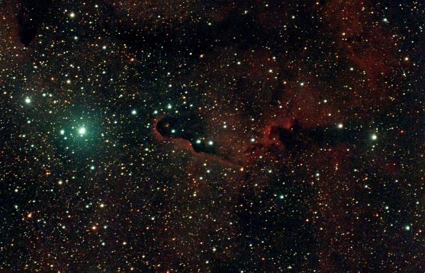 Close-up of the Elephant's Trunk: a dark curling column of dust with a glowing red rim, beside a blue-white star cluster