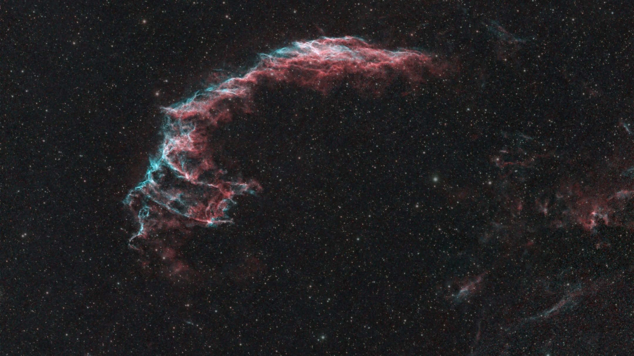 The Eastern Veil Nebula, a curved filament of red hydrogen and teal oxygen gas against a dense star field
