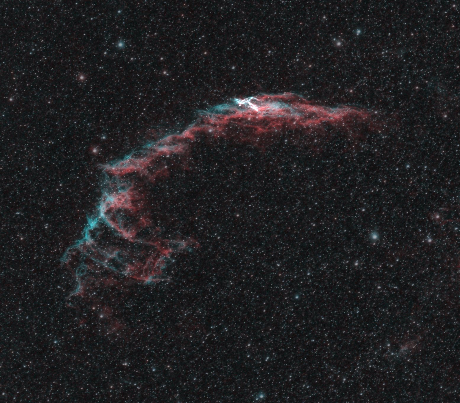 The Eastern Veil Nebula, a curved filament of red hydrogen and teal oxygen gas against a dense star field
